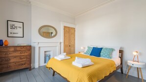 A bedroom with a bed, a dresser, a mirror, a fireplace, and a wall with a framed quote. - Oyster Shore -  a Bloom Stays holiday let that sleeps 8 guests  in 3 bedrooms (Whitstable)
