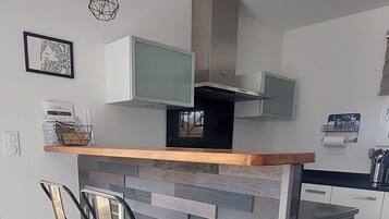 Una cocina moderna con una isla central, dos sillas, iluminación colgante y un microondas.