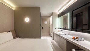 Una camera d'hotel moderna con un letto grande, un bagno con un'area trucco e uno specchio ampio.