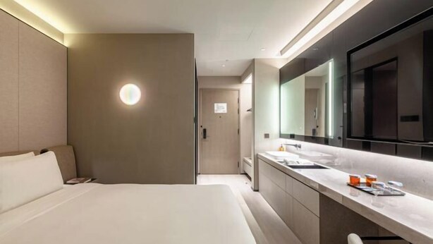 A modern hotel room with a large bed, a bathroom with a vanity, and a large mirror. - Orange Hotel (Beijing Wangjing Subway Station) (Beijing)
