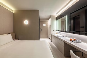 A modern hotel room with a large bed, a bathroom with a vanity, and a large mirror.