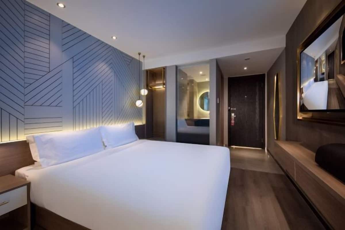 A modern hotel room with a large bed, a built-in desk, and a large mirror.