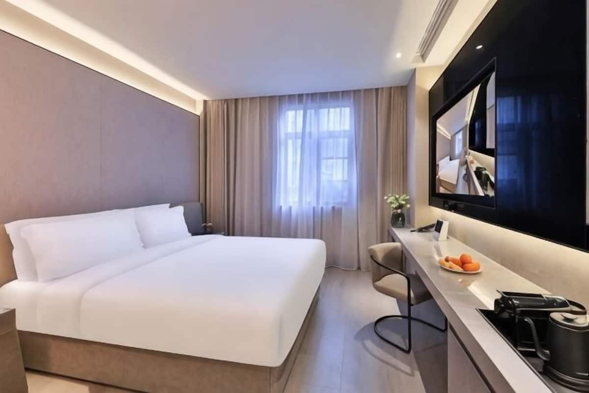 A modern hotel room with a large bed, a desk with a chair, a flat-screen TV, and a window with curtains.
