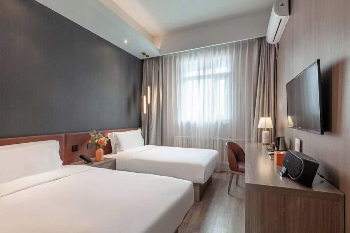 A hotel room with two beds, a desk, a chair, a TV, and a window with curtains.
