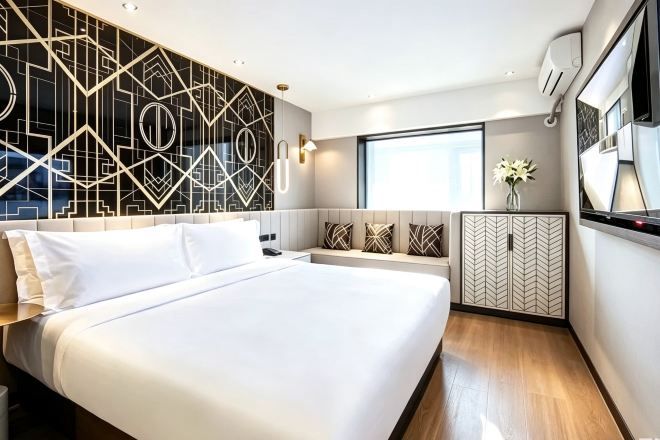 Une chambre d’hôtel moderne avec un grand lit, un motif géométrique sur le mur, un coin salon et une fenêtre.