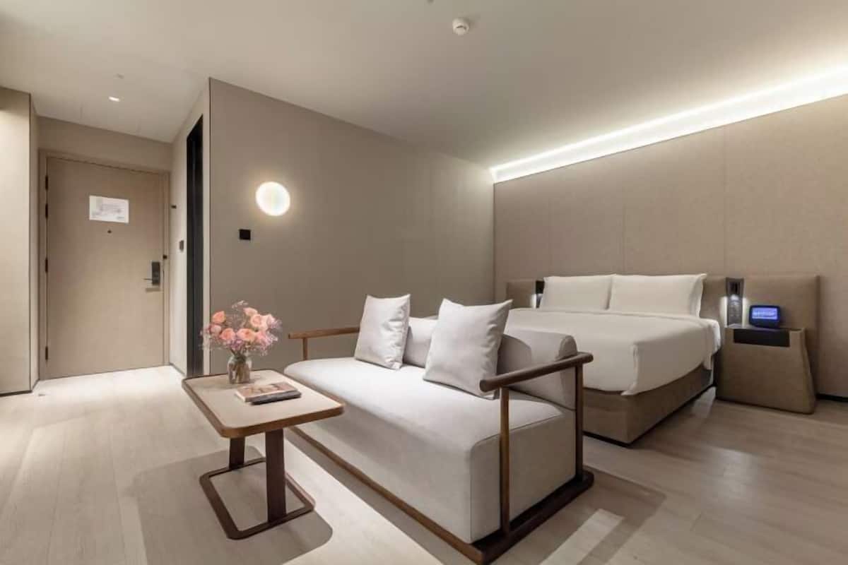 A modern hotel room with a bed, a sofa, a bedside table, and a small desk.