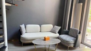 Un soggiorno moderno con divano e poltrona, un tavolino rotondo e una finestra con tende.