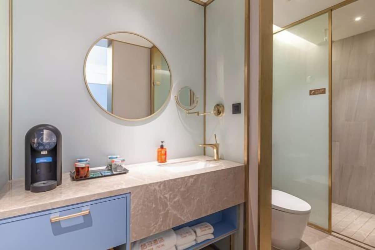 A modern bathroom with a round mirror, a coffee machine, a sink, and a toilet.