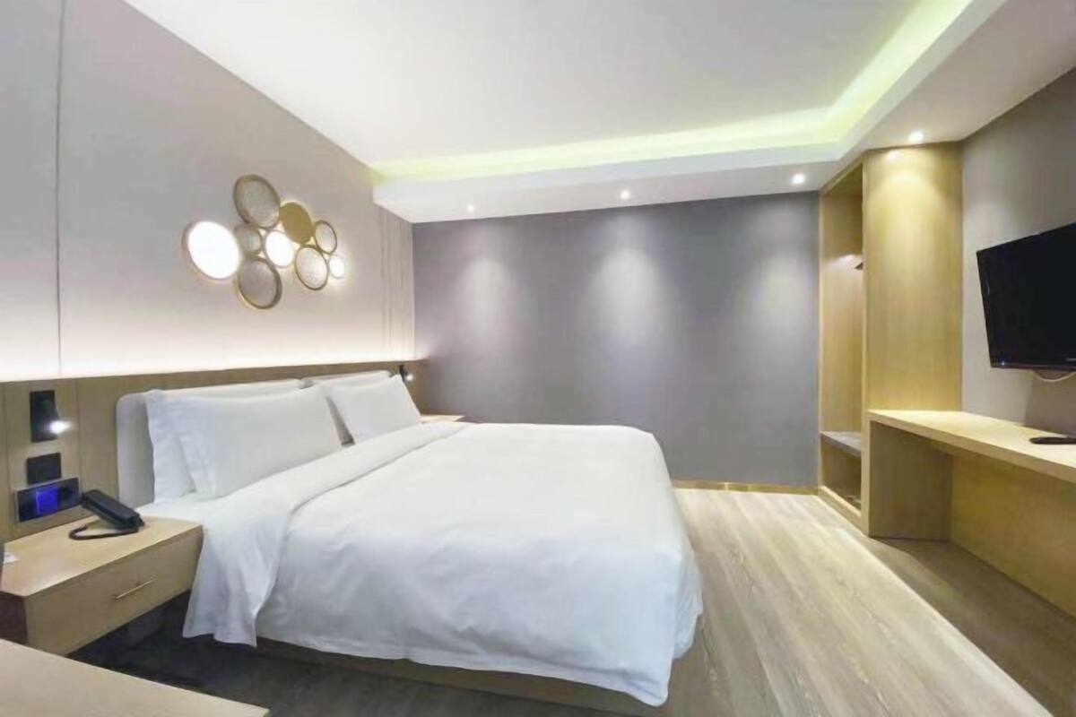 A modern hotel room with a large bed, bedside tables, a flat-screen TV, and a wall-mounted light fixture.