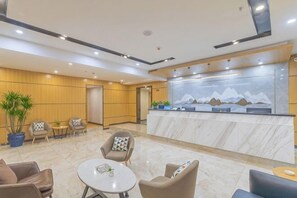 Een hotellobby met een receptiebalie, zithoek en een groot raam met uitzicht op de bergen.