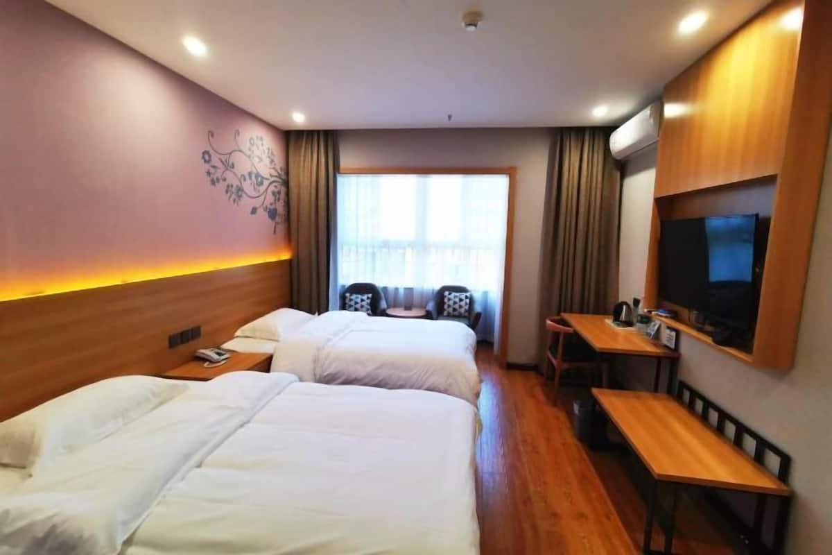 Habitación de hotel con dos camas, un escritorio, una silla, un televisor y una ventana con cortinas.