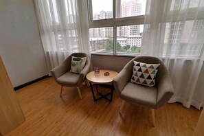 Een kamer met twee fauteuils, een kleine ronde tafel en een uitzicht op gebouwen door grote ramen.