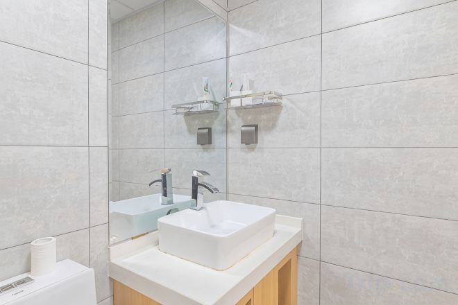 A modern bathroom with a white sink, two faucets, a mirror, and a towel rack.