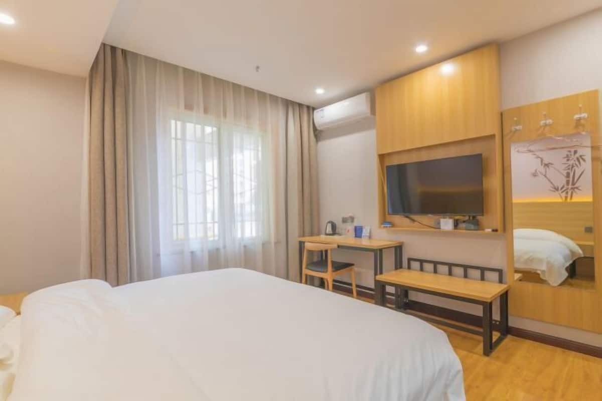 Habitación de hotel con cama, escritorio, silla, televisor y espejo.