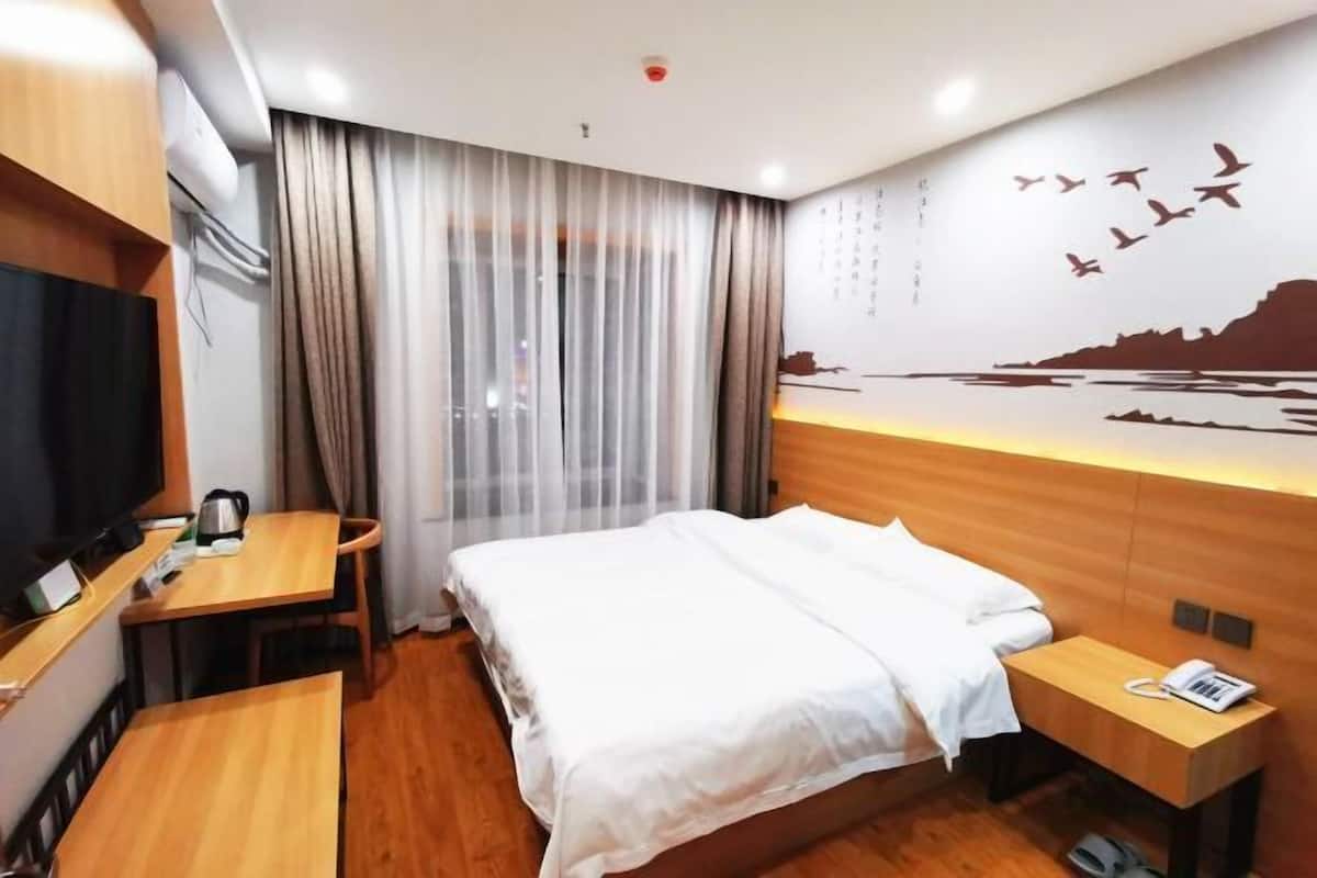 Habitación de hotel con cama, escritorio, silla, televisión y un mural de un pájaro en la pared.