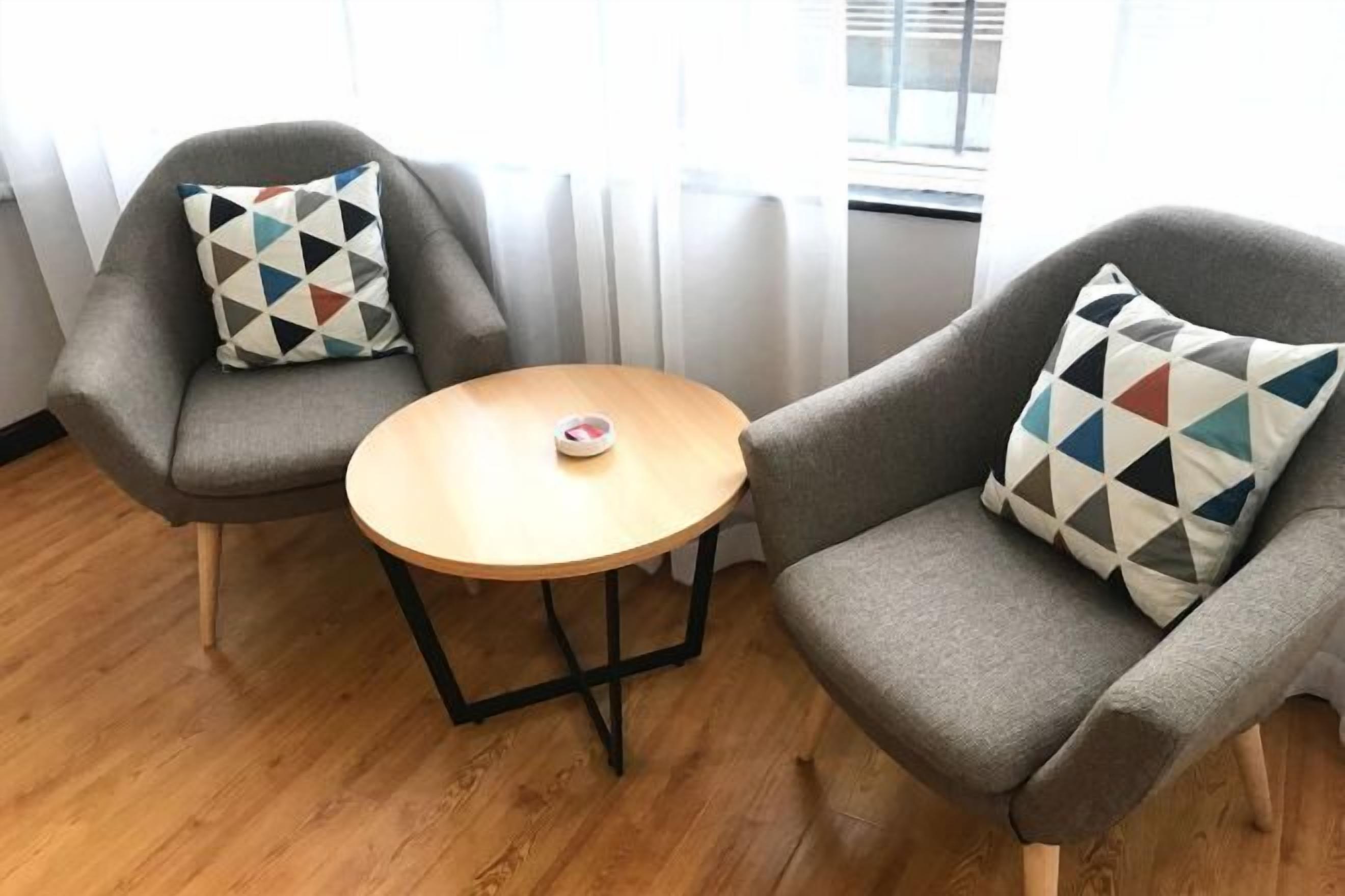 Two grey armchairs with patterned cushions, a small round wooden table, and a window with curtains.