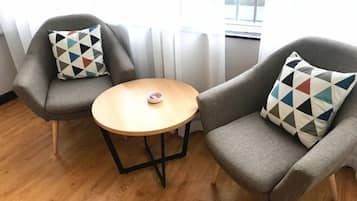 Two grey armchairs with patterned cushions, a small round wooden table, and a window with curtains.