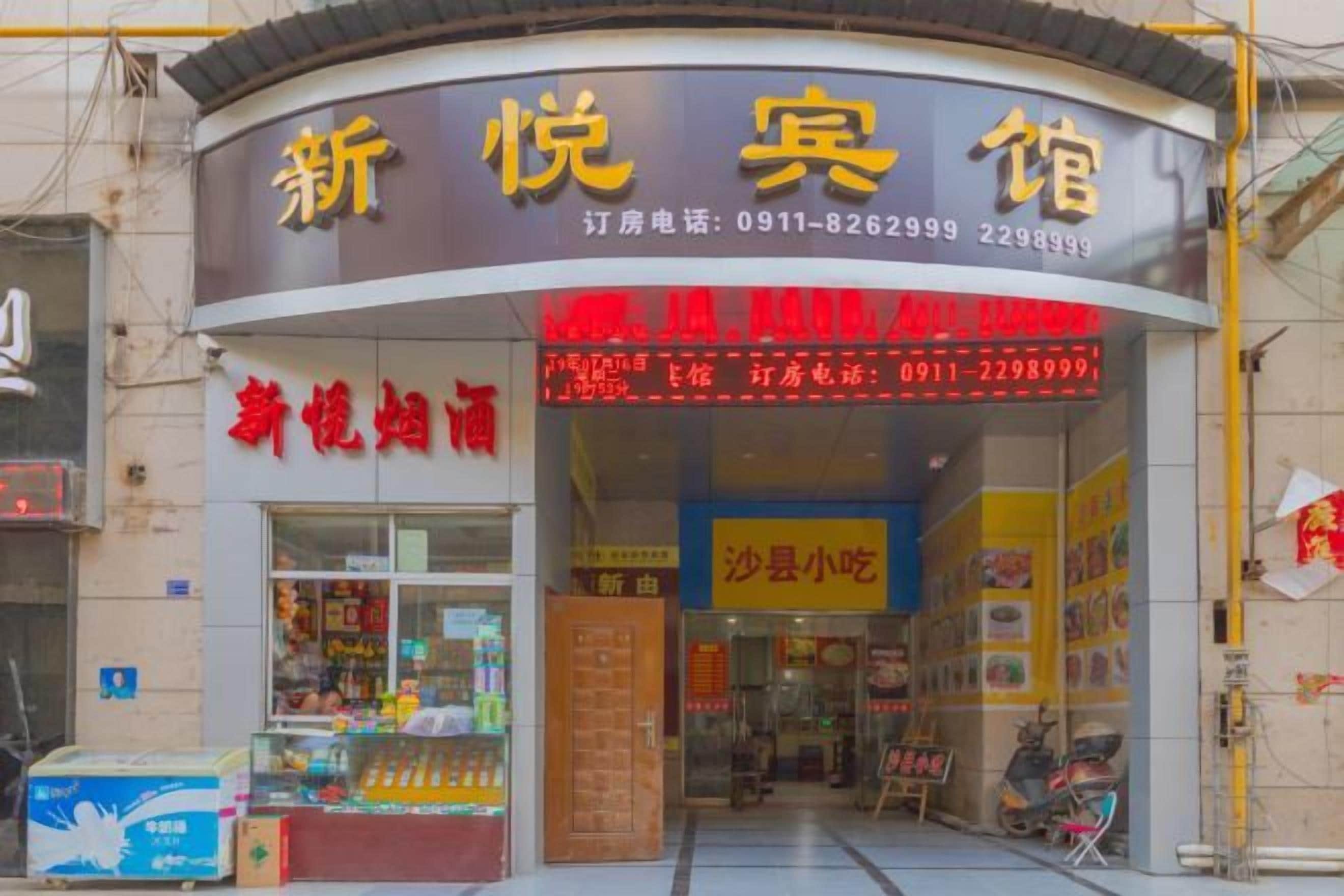 A storefront with a sign indicating a restaurant or cafe. There is a display window with various items, possibly food or merchandise. The entrance has a glass door, and there are steps leading up to the door.