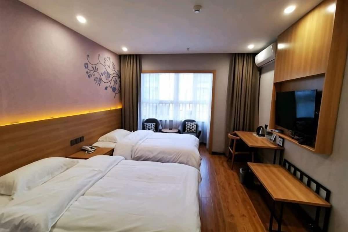 Habitación de hotel con dos camas, un escritorio, una silla, un televisor y un ventanal con cortinas.