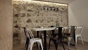 Zona pranzo con parete in pietra, tavolo bianco e sedie in metallo.