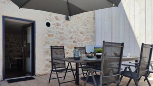 Patio esterno con tavolo e sedie, una pianta in vaso e un barbecue.