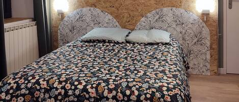 Un dormitorio con colcha estampada, cabecero de madera, dos lámparas de pared y una lámpara colgante.