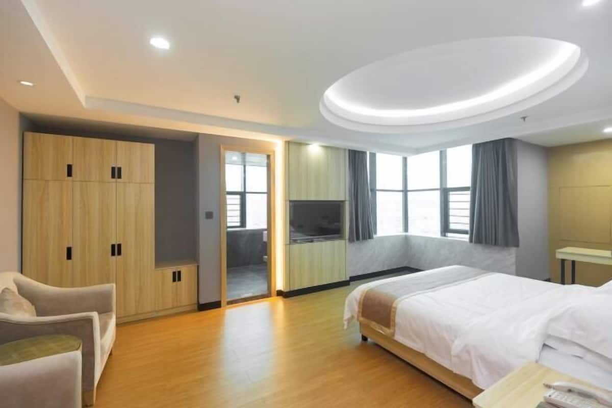 Quarto de hotel moderno com cama, área de estar, guarda-roupa e televisão.
