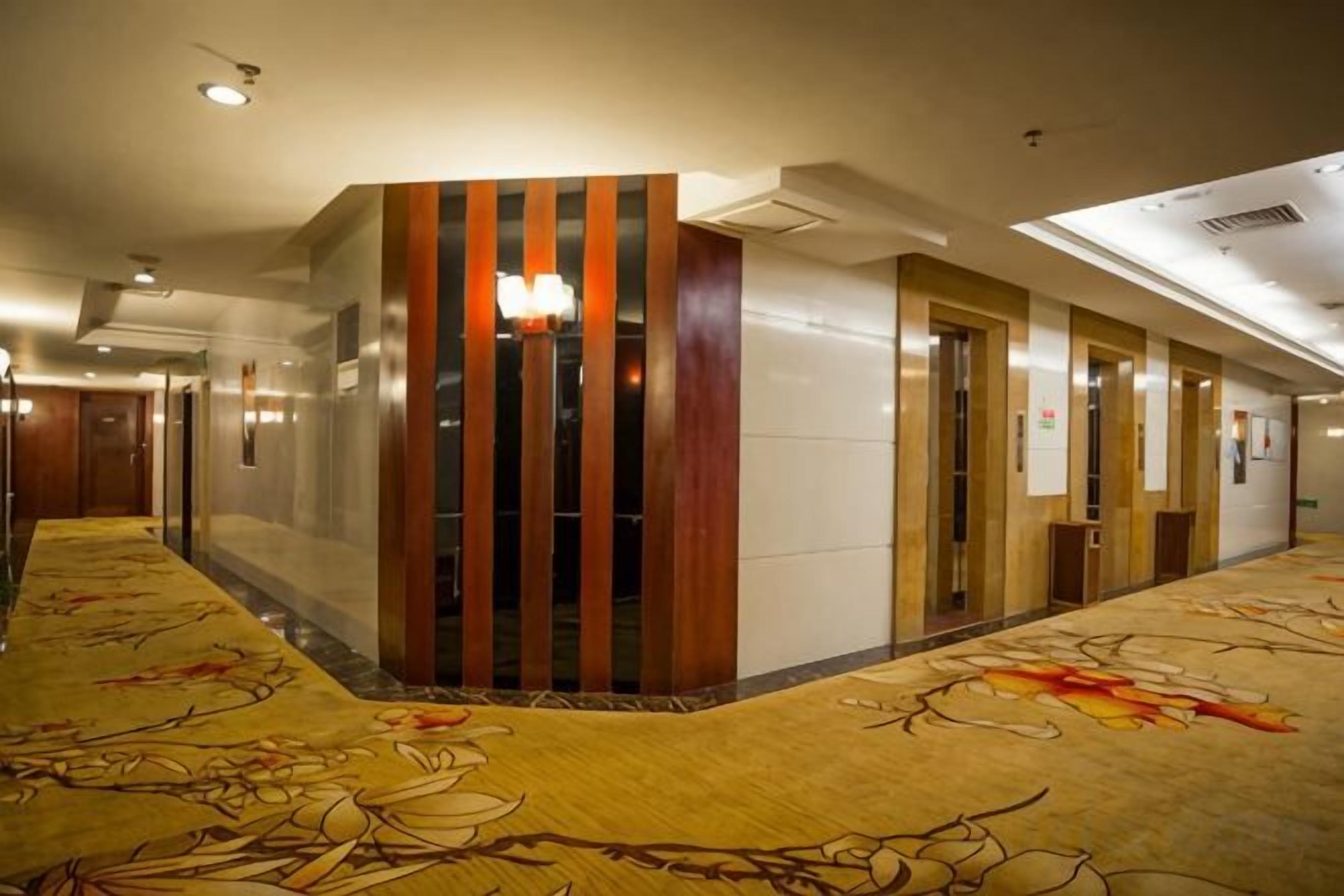 A hotel corridor with a patterned carpet, wooden paneling, and doors leading to rooms.