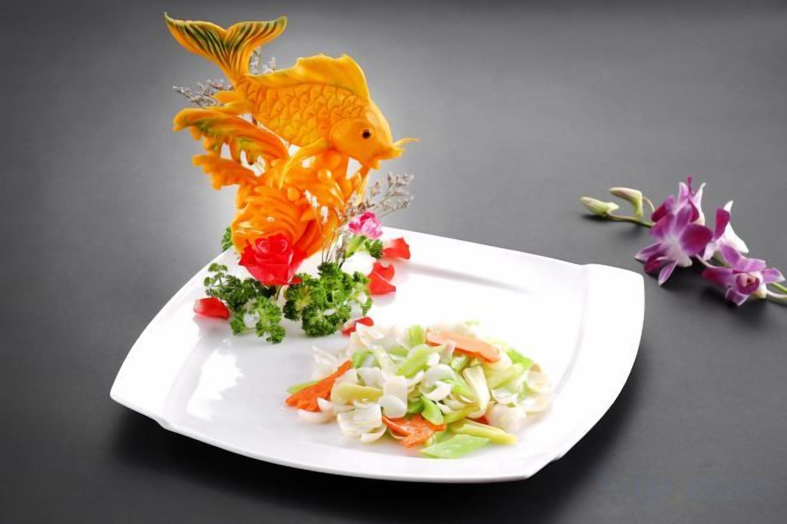 Un plato blanco con un alimento con forma de pez, ensalada y flores moradas.