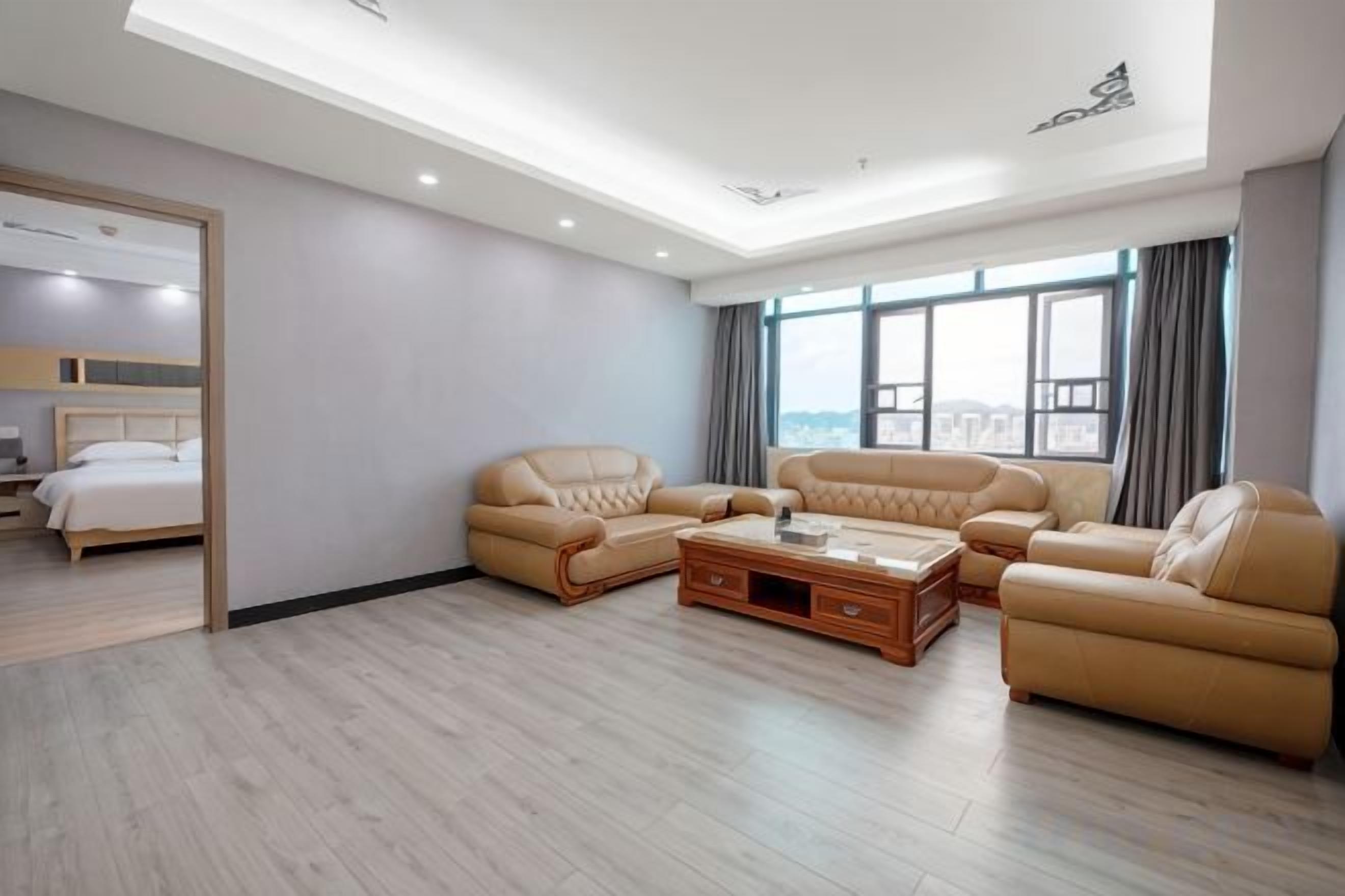 A modern hotel room with a large bed, two sofas, a coffee table, and a view of the city.