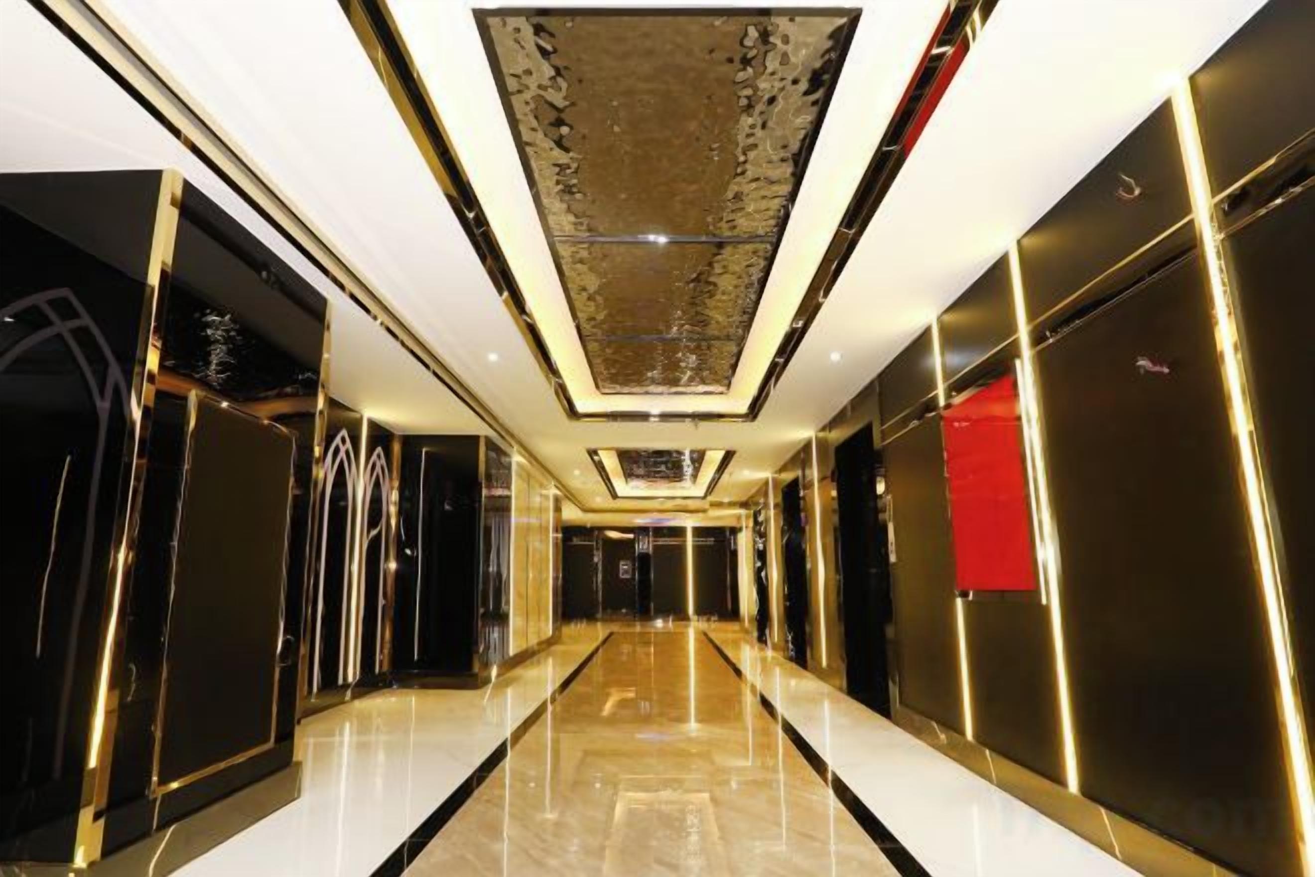 A hallway with a reflective floor, a patterned ceiling, and a red accent wall.