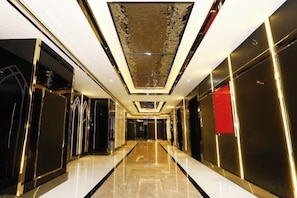 A hallway with a reflective floor, a patterned ceiling, and a red accent wall. - Baohua Hotel (Chaozhou)