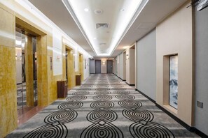 A hotel corridor with a patterned carpet, doors, and a framed artwork on the wall. - Baohua Hotel (Chaozhou)