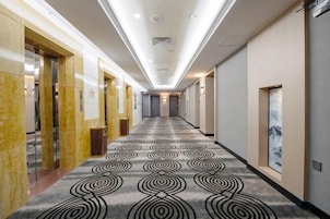 Un pasillo de hotel con alfombra estampada, puertas y una obra de arte enmarcada en la pared.