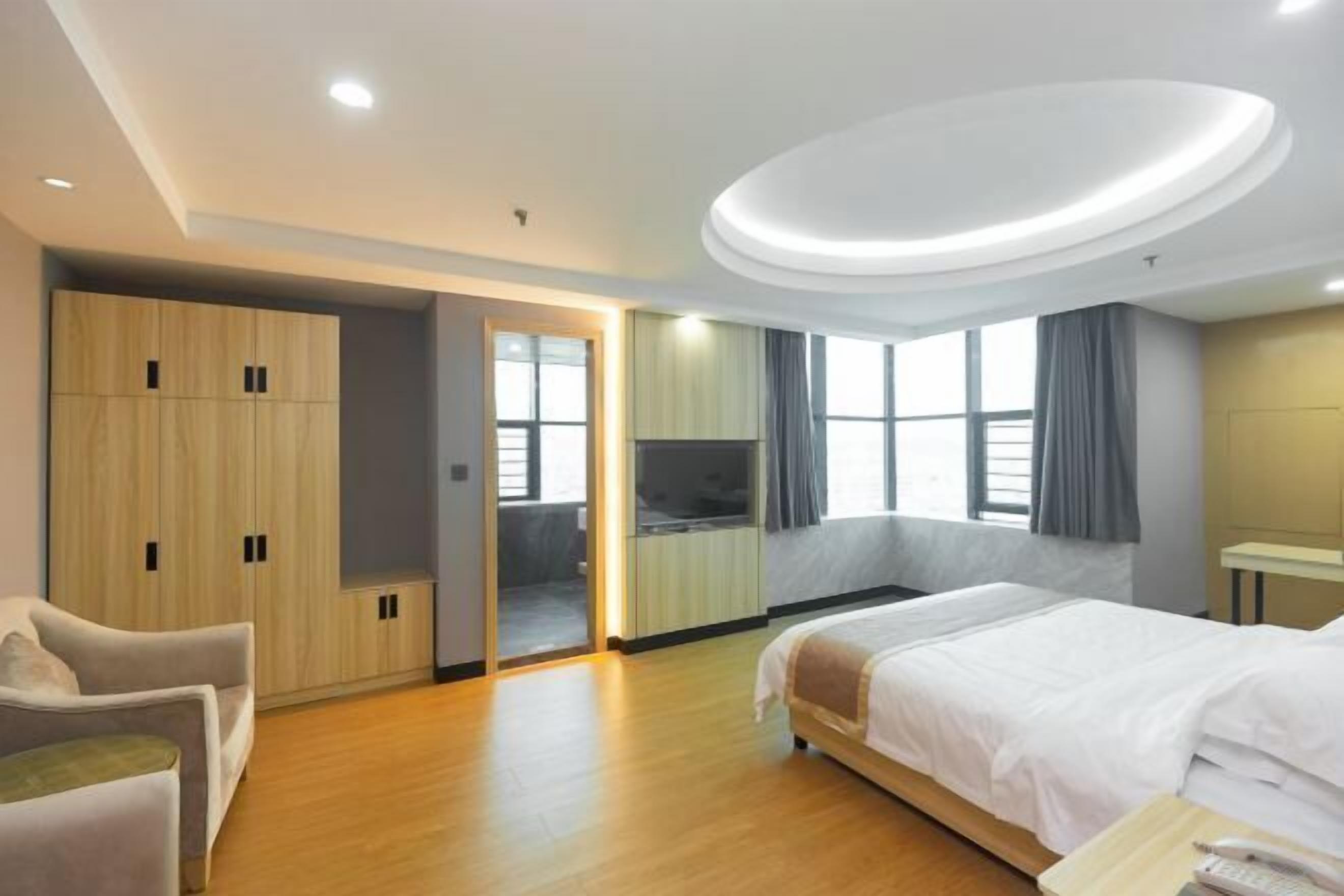 A hotel room with a bed, a seating area, a wardrobe, and a television.