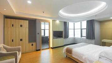 A hotel room with a bed, a seating area, a wardrobe, and a television.