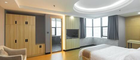 A hotel room with a bed, a seating area, a wardrobe, and a television.