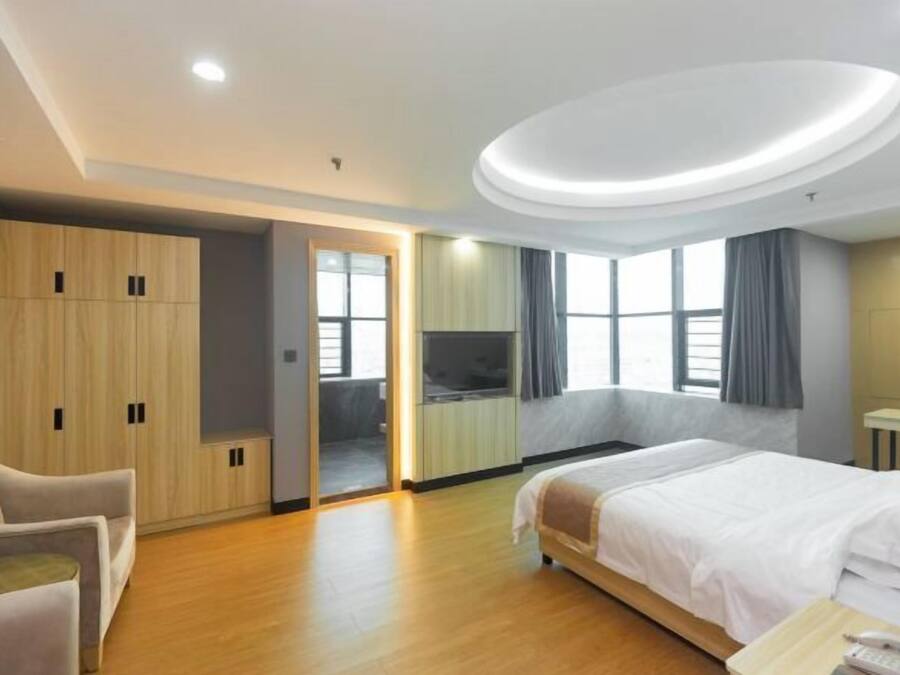 A hotel room with a bed, a seating area, a wardrobe, and a television.