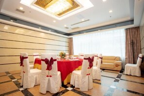 Une salle de conférence avec une table ronde, des chaises blanches ornées de rubans rouges et un lustre.
