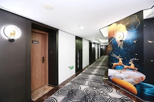 Un pasillo con alfombra estampada, una puerta de madera y un mural con motivos celestiales.