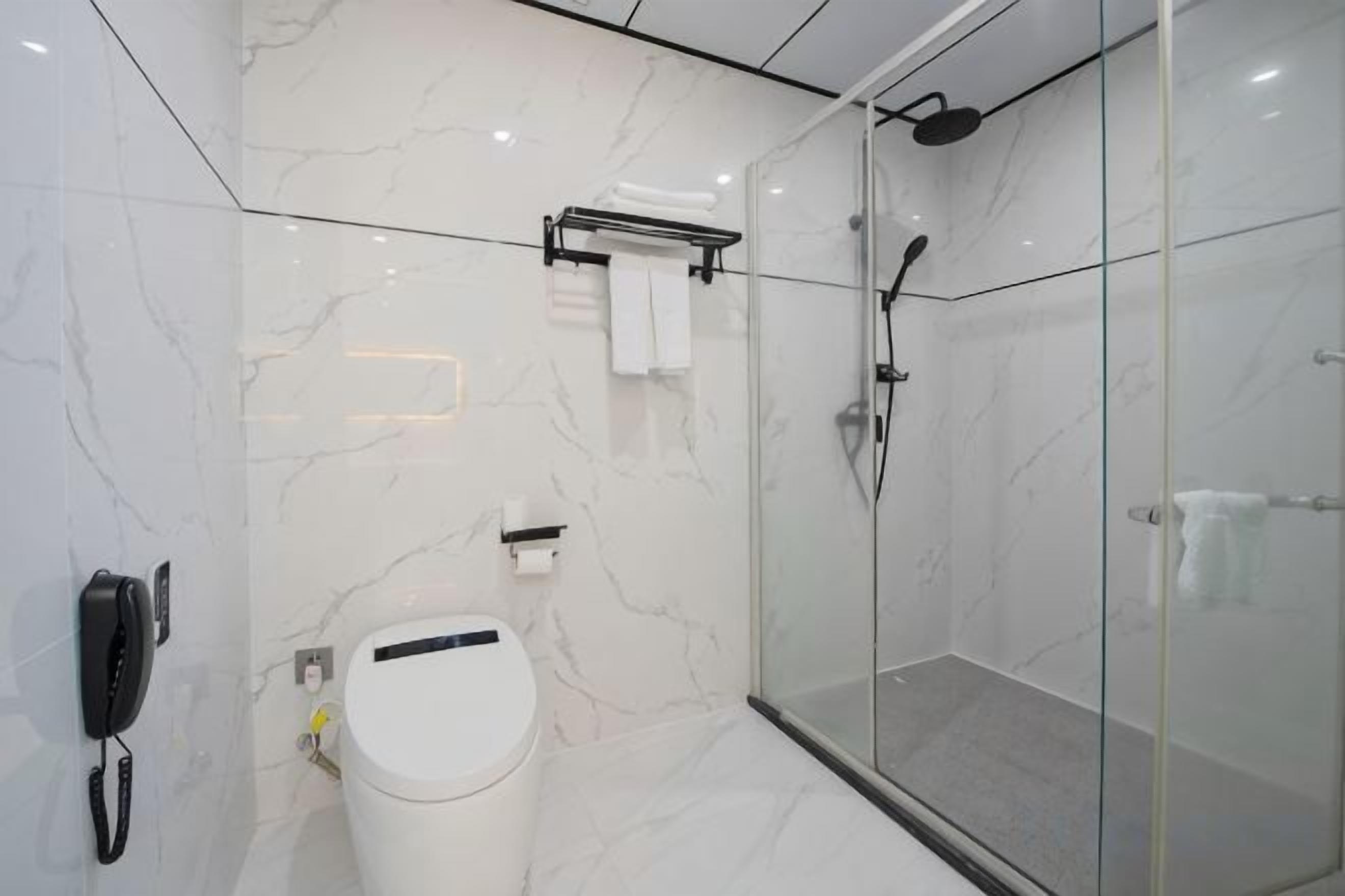 A modern bathroom with a toilet, a glass shower enclosure, and a marble wall.