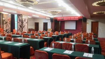A conference room with rows of tables and chairs, a projector screen, and a red banner.
