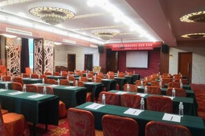 Une salle de conférence avec des rangées de tables et de chaises, un écran de projection et une banderole rouge.