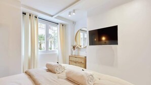 Un dormitorio con cama, cómoda, espejo y televisor montado en la pared.