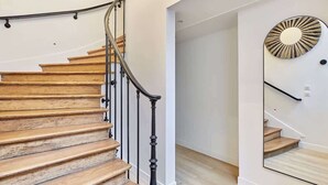 Una escalera de madera con barandilla negra y un espejo adosado a la pared que refleja la escalera.