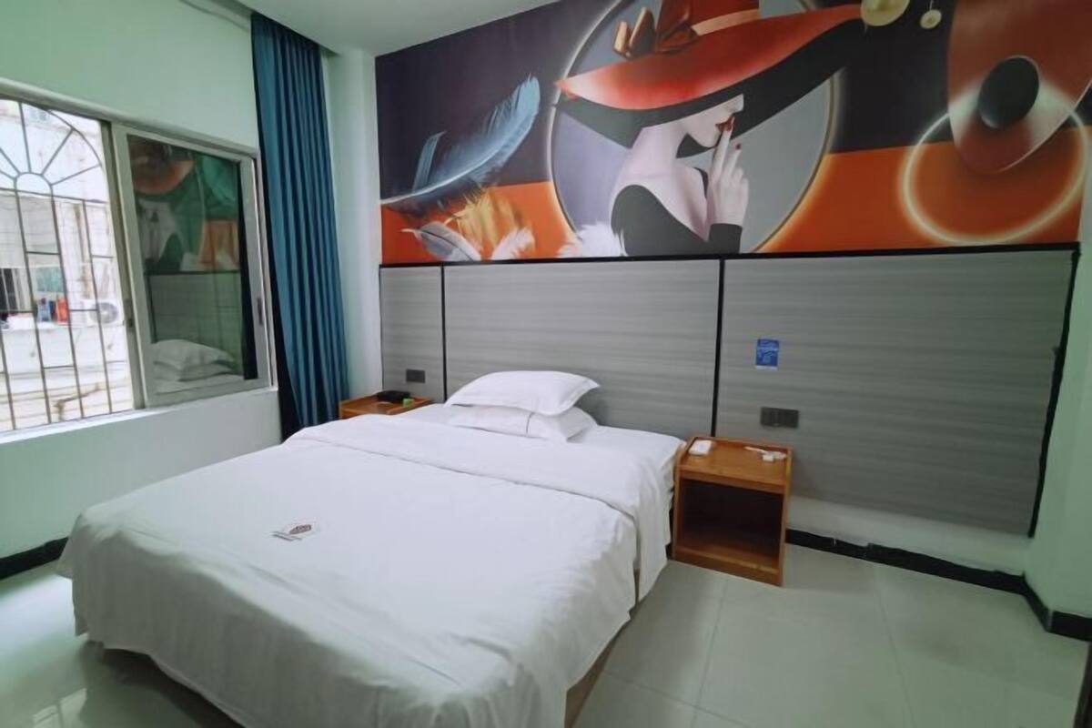 A hotel room with a bed, a nightstand, a window with curtains, and a wall mural.