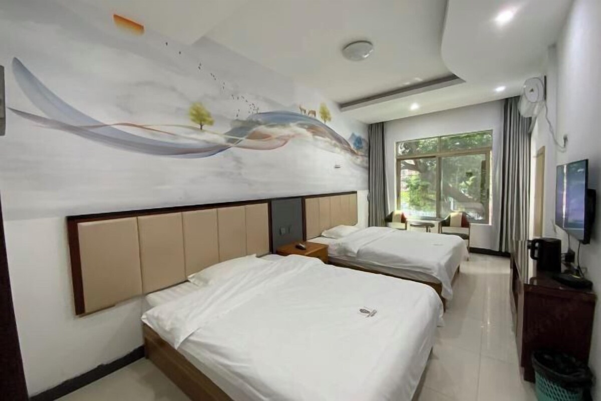 A hotel room with two beds, a mural on the wall, a TV, and a window with a view of greenery.