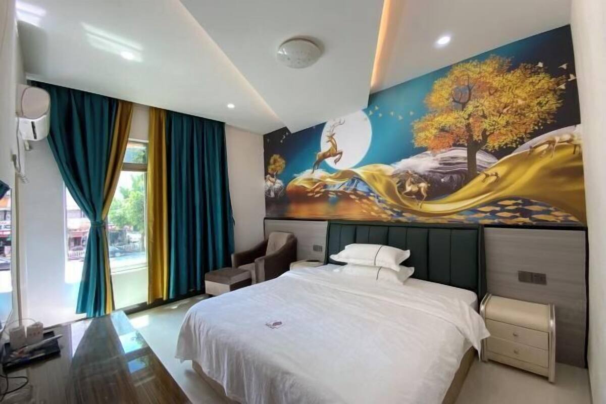 A hotel room with a bed, a desk, a chair, a nightstand, and a large wall mural.