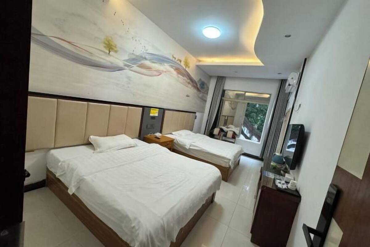 A hotel room with two beds, a mural on the wall, a television, and a window with a view.