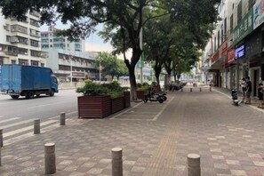 A sidewalk with bollards, a blue truck on the road, and buildings with signage. - Fogang Xingshu Fashion Hotel (Fogang)